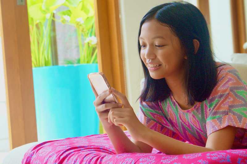 A young girl laying on the bed while using her cell phone