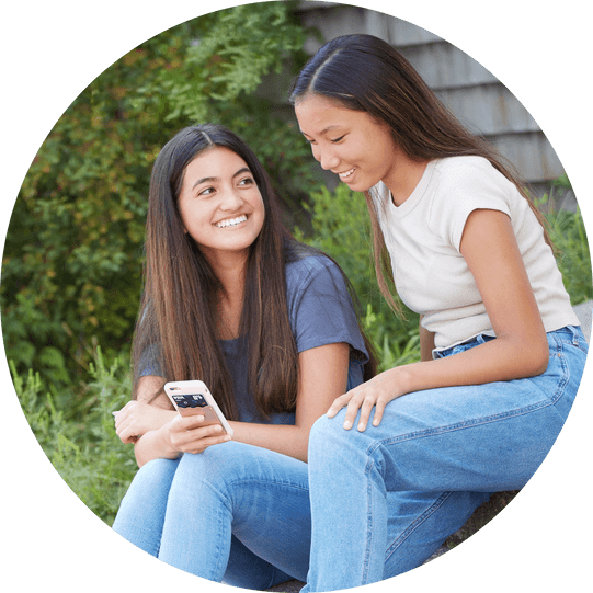 Two smiling teenagers looking at a phone showing the Till Financial app