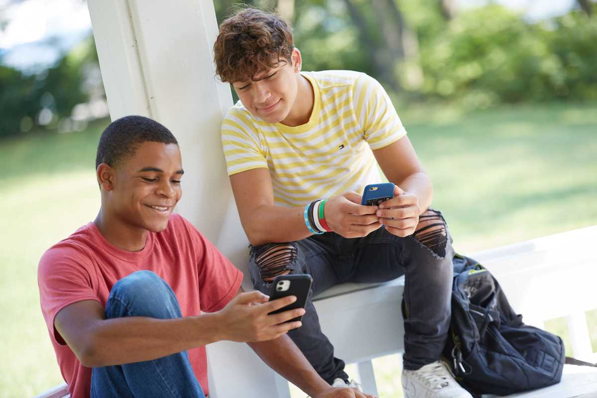 Two teenagers smiling while looking at their phones
