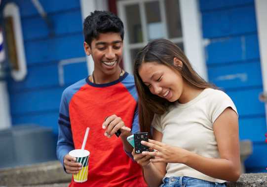 Two smiling teenagers looking at a phone showing the Till Financial app